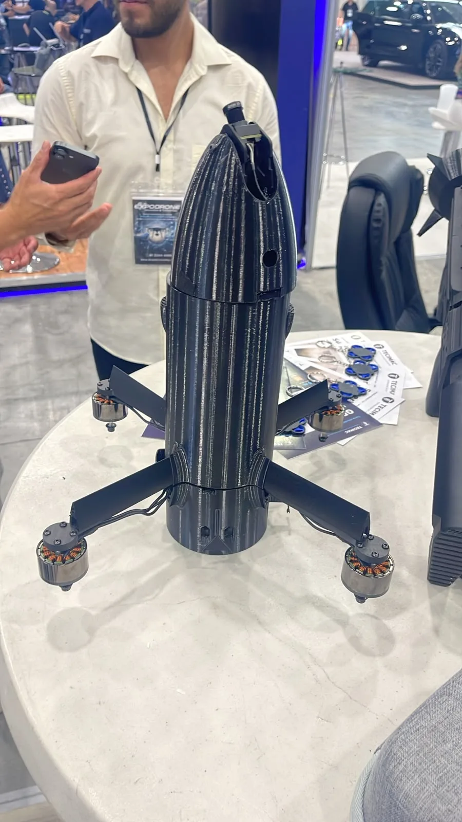 Multicóptero de fuselaje cilíndrico con cuatro brazos plegables, sobre la mesa del stand